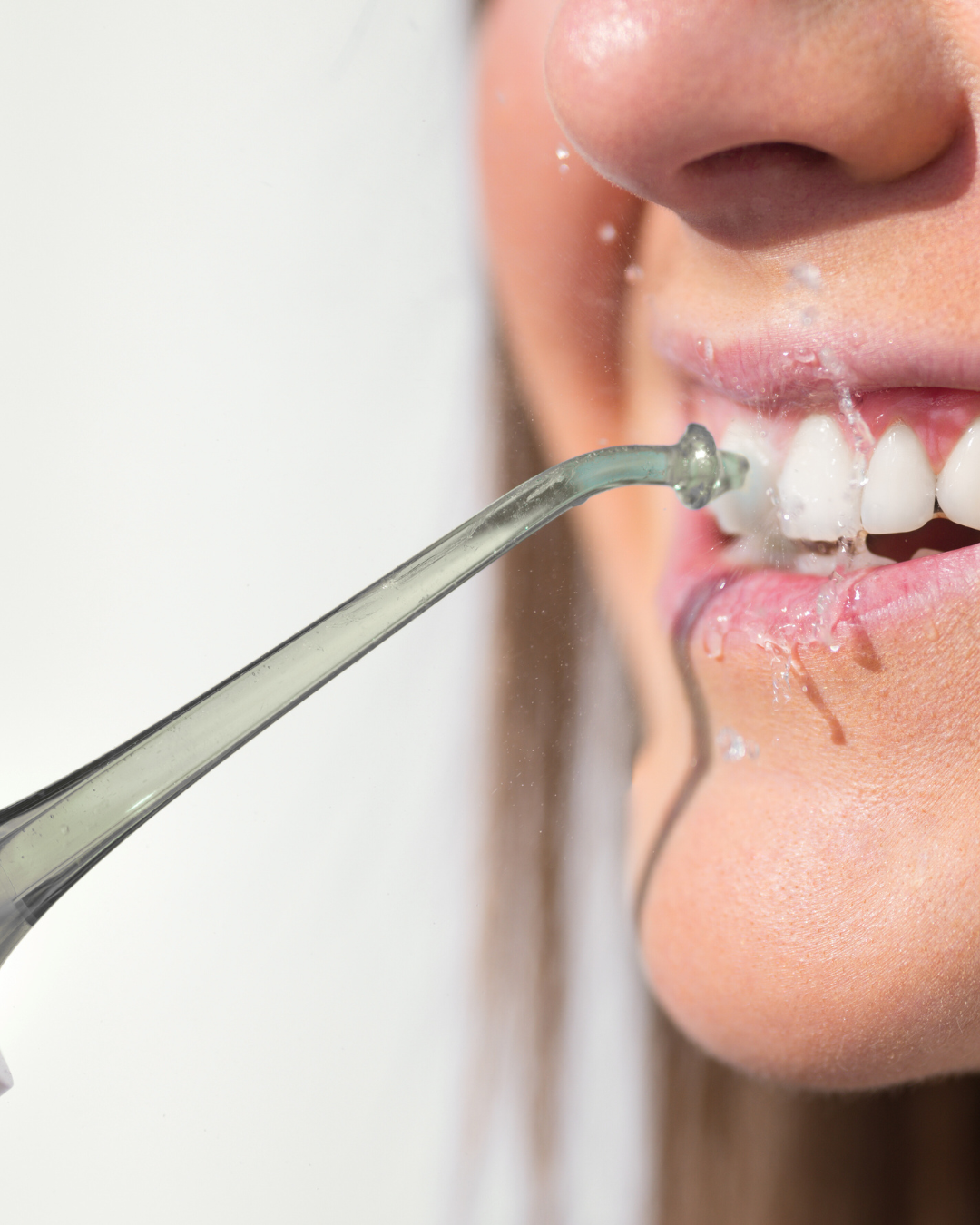 Close-up of a woman using an ozone water flosser, with a stream of water cleaning between her teeth for improved oral hygiene.