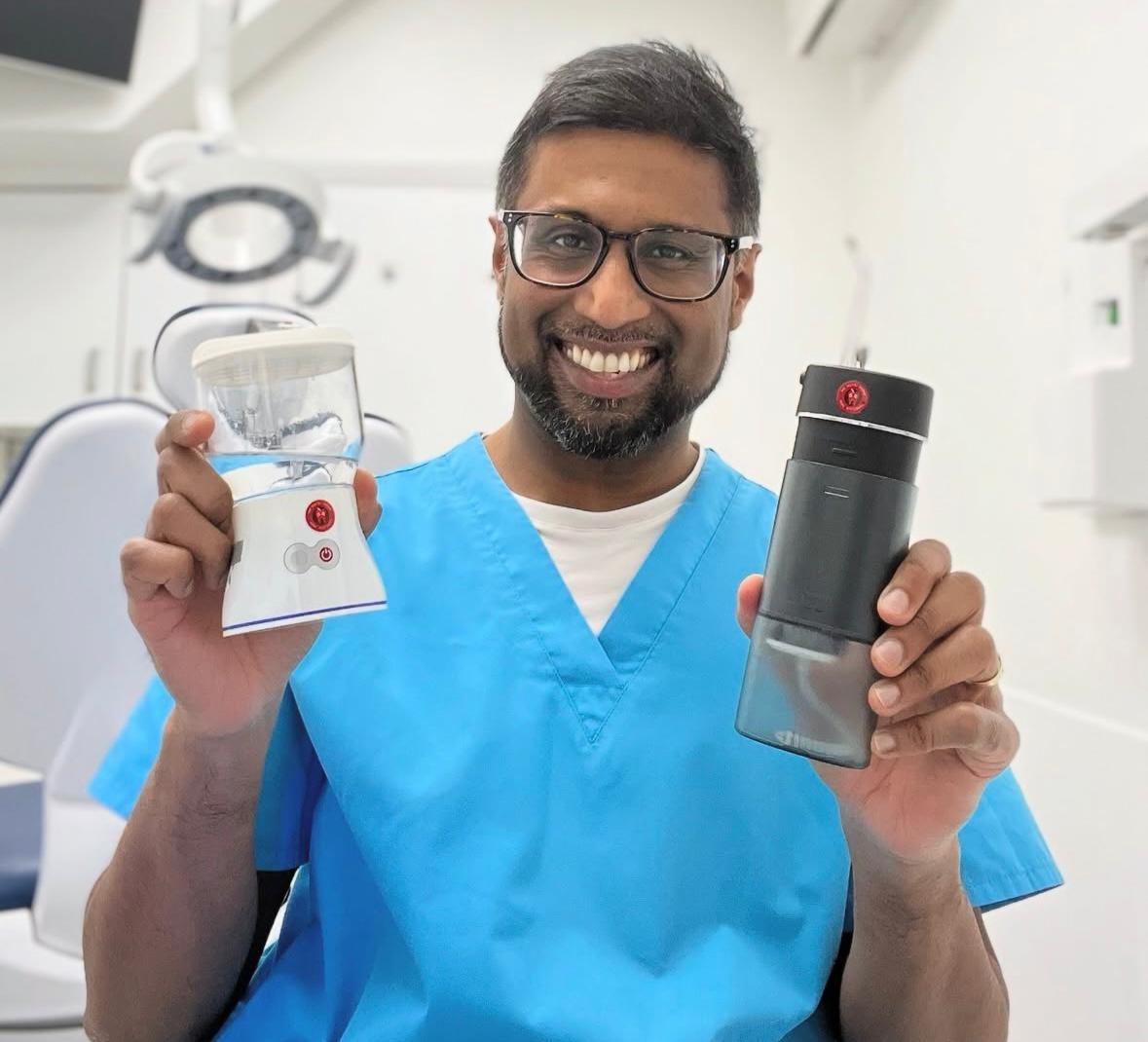 Smiling dentist in blue scrubs holding two ozone water flossers in a bright clinical setting, showcasing advanced tools for holistic dental care.